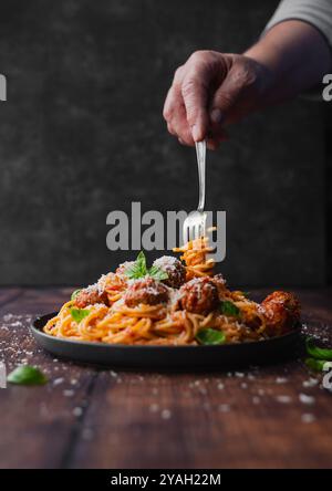 Hand twirling fork in plate of spaghetti and meatballs on table. Stock Photo