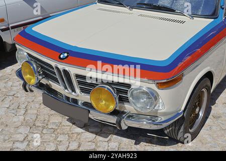 Classic bmw 2002 with racing stripes parked on a sunny cobblestone ...