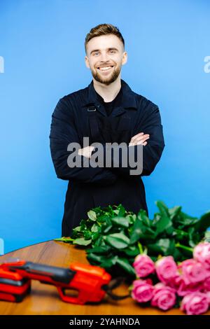 Man in apron cuts off the ends of a rose on blue background. Stock Photo