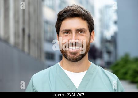 Smiling bearded man doctor in uniform standing outdoor medical center Stock Photo
