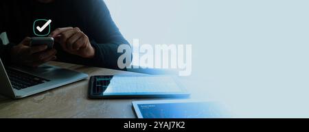 A man uses a smartphone, surrounded by digital devices displaying data analytics and graphs, with a checkmark symbol above. Stock Photo