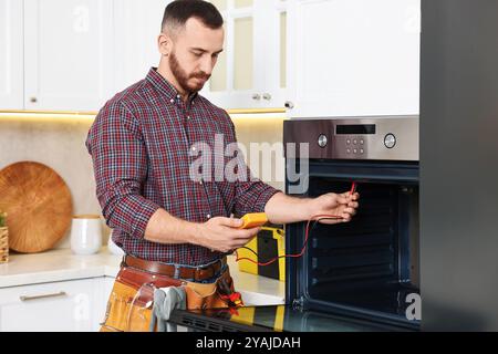 Repairman testing oven element with multimeter in kitchen Stock Photo