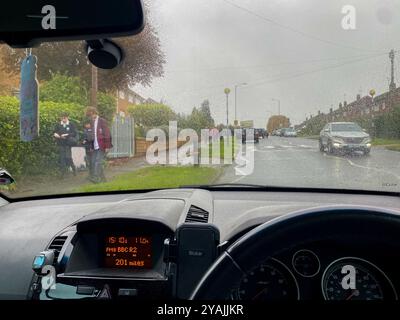 View looking forward from a parked car waiting to pick children up from school at the end of the school day on a wet day in October in Reading, UK Stock Photo