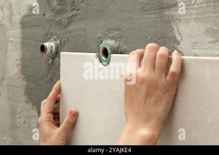 Woman tiling bathroom walls, applying adhesive on a tile and placing ceramic tile in right position. Process of installation of tiles in the bathroom Stock Photo