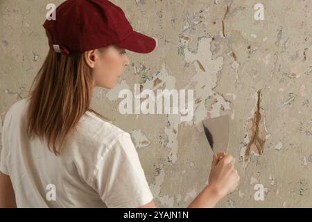 Woman plastering wall with putty-knife. Fixing wall surface and preparation for painting. DIY housing improvement project. Stock Photo