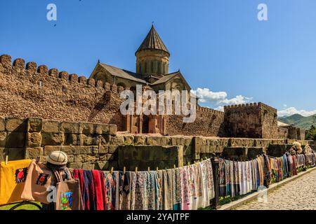 market traders hang colourful textiles on railings in front of the imposing svetitskhoveli cathedral a UNESCO world heritage site in mtskheta georgia Stock Photo