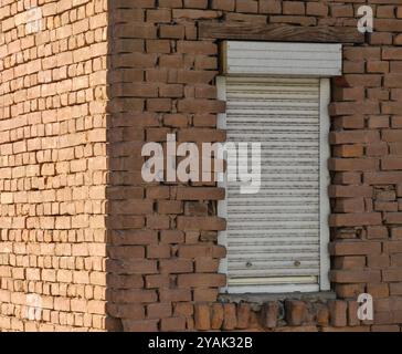 Around the Corner: Closed Window with White Blinds and Brick wall background. Light and shadow, contrast. Stock Photo