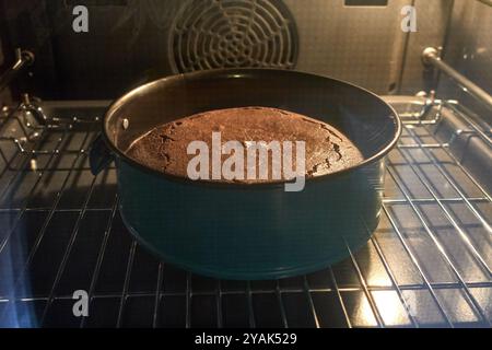 A homemade chocolate cake in a round metal pan is baking on a tray inside the oven, visible through the glass door Stock Photo