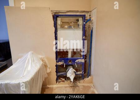 Wall under construction showing the internal cistern of a bathroom in a house with the bidet covered with plastic to protect it Stock Photo