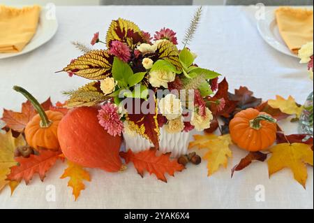 Holiday harvest themed Thanksgiving table centrepiece dinner arrangement with pumpkins, gourds, leaves, and flower bouquets Stock Photo