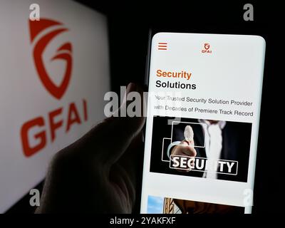 Person holding cellphone with webpage of Singaporean technology company Guardforce AI on screen with logo. Focus on center of phone display. Stock Photo