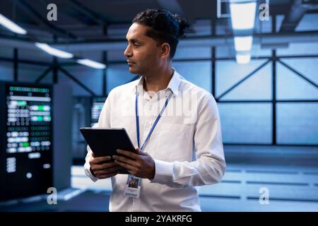 Manager overseeing server room, walking around with tablet, troubleshooting hardware mainframes. Supervisor doing inspection in server farm, monitoring energy consumption across rigs with digital device Stock Photo