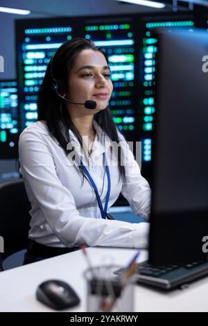 Cheerful data center operator supporting engineering team doing equipment maintenance, talking in headset microphone. Smiling person in server room coordinating technicians using mic Stock Photo