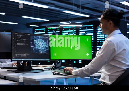 System administrator doing checkup on green screen computer in server hub used for artificial intelligence workloads. IT expert inspecting neural network data center with chroma key PC Stock Photo