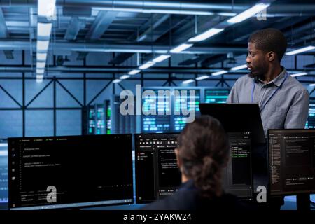African american man doing routine maintenance in data center to extend equipment life span and avoid downtime. Employee monitoring supercomputers for issues such as overheating or power fluctuations Stock Photo