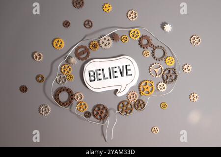 Woman holding paper in hand spelling words Believe with blue background. Torn piece of paper with the word believe in the woman's palms. Stock Photo