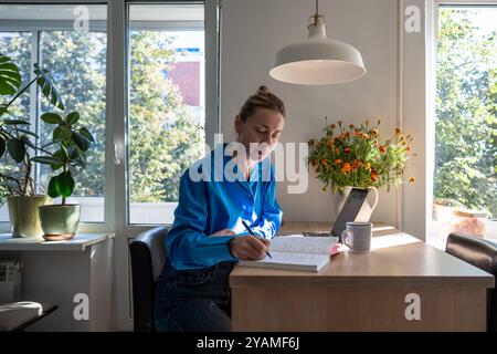 Person writing notes in a planner next to a laptop and coffee Stock ...