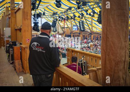 Man in security jumper standing in front of a busy event in a tent, Canstatter Wasen, Stuttgart, Germany, Europe Stock Photo