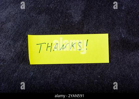 A yellow sticky note displaying the word Thanks on a textured dark background, conveying gratitude and appreciation Stock Photo