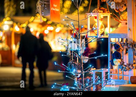 View of the tree with lights and lanterns as blurry illuminated kiosks on background at Christmas market in Asti, Italy. Stock Photo