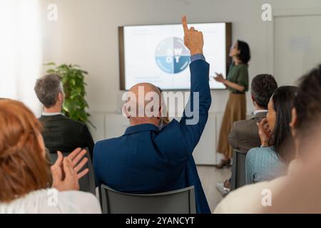 Engaged participant raising hand during SWOT analysis presentation. Diverse business team in modern office setting. Image conveys active participation Stock Photo