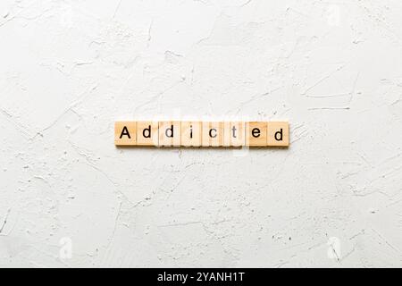 Addicted word written on wood block. Addicted text on cement table for your desing, Top view concept. Stock Photo