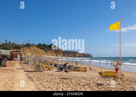 Lagos, Algarve, Portugal - October 18, 2023: People at Praia de Porto de Mos beach at the Atlantic Ocean with yellow flag in sand. Stock Photo