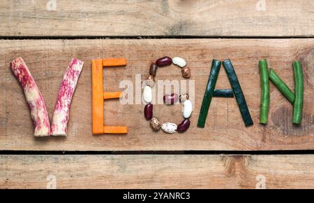 The word "Vegan" written with vegetables, fruits, nuts and legumes on rustic wooden background, concept - organic ingredients for healthy vegan food a Stock Photo