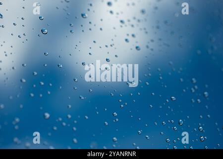 Water droplets on glass window. Blue sky and white clouds in the background, close up macro shot. Stock Photo