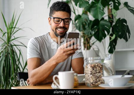 Young black man eating breakfast and reading the news online. Handsome man using mobile phone Stock Photo
