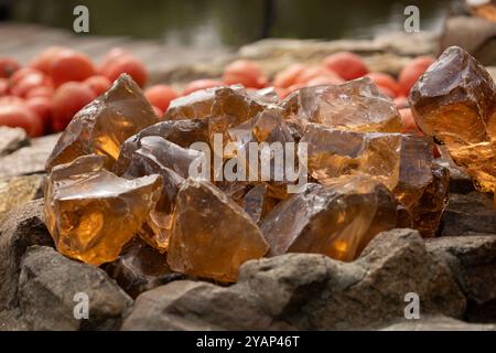 Close-up of translucent amber-colored crystals on a bed of rocks with pumpkins in the background on a sunny day Stock Photo