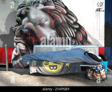 Ein Obdachloser schläft unter dem Wandbild eines schlafenden Löwen auf einer Bank der S-Bahn-Station *Möllerbrücke* in Dortmund, 15.10.2024 *** A homeless man sleeps under the mural of a sleeping lion on a bench at the S-Bahn station Möllerbrücke in Dortmund, 15 10 2024 Stock Photo