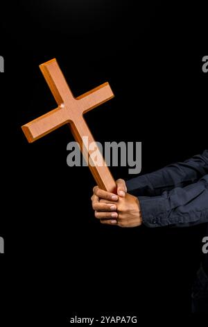 Man holding a wooden religion cross in his hand on black background. Symbol of faith and worship in God. People christianity prayer in church. Religio Stock Photo