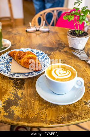 A Caffe Latte art and a croissant, served on a rustic wooden table. Stock Photo