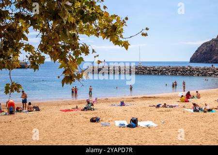 Holidaymakers and people sunbathing on vacation on the man made beach in Machico the second largest town / resort on the Portuguese Island of Madeira Stock Photo