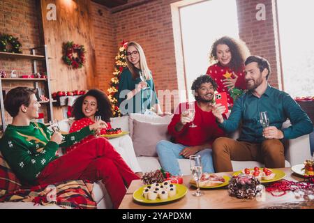 Photo of cheerful young people friends group sit couch enjoy celebrate cozy christmas party decor spacious apartment indoors Stock Photo