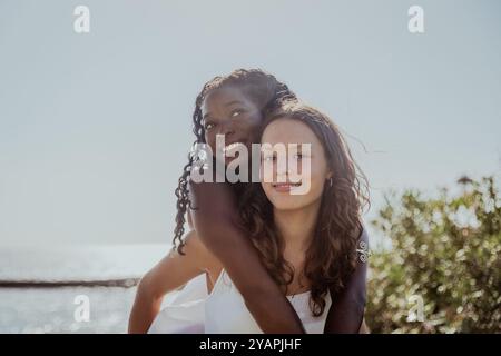 Two young women are hugging each other on a beach, diverse friends spending summer together Stock Photo