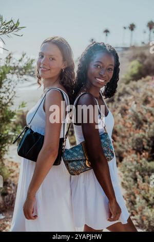 Two friends are standing back to back, both wearing white dresses, diversity concept. Stock Photo