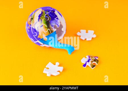 Blue dinosaur hatching from a puzzle globe with scattered puzzle pieces on a bright orange background, symbolizing interactive learning. Stock Photo