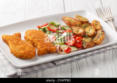 Delicious food breaded white fish with fresh salad and fried potatoes close-up in a plate on a wooden table. Horizontal Stock Photo