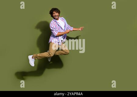 Full size photo of funny guy dressed striped shirt brown pants jumping indicating at sale empty space isolated on khaki color background Stock Photo