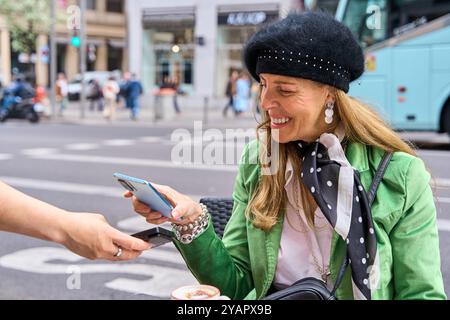 Woman paying bill through smartphone using NFC technology in a restaurant. Satisfied customer paying through mobile phone using contactless technology Stock Photo