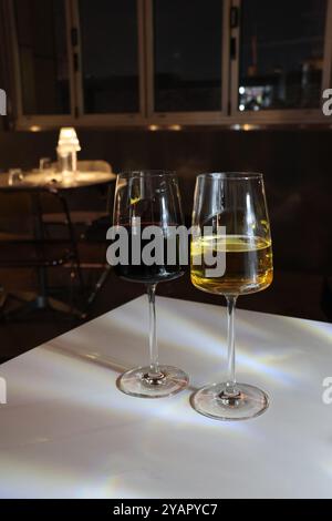 Two wine glasses, one red and one white, sit on a table. The red wine is almost gone, while the white wine is almost full. The glasses are placed next Stock Photo