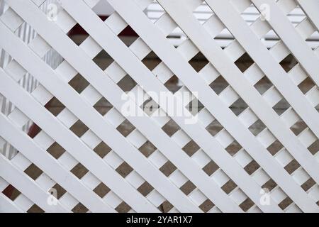 Close-up of a white lattice fence with diagonal wooden slats creating a geometric pattern. Simple but elegant architectural detail. Stock Photo