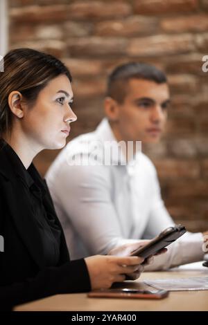 Two young professionals, a man and a woman, engage intently in a business meeting in an office with a rustic brick backdrop, portraying a modern profe Stock Photo