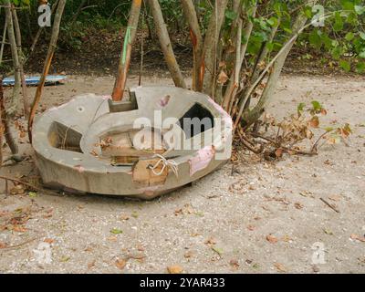 Slotted Concrete base buoy holder washed up on sand after a hurricane Helene and Milton. Metal Pole up in air against mangrove trees. Laying on sand w Stock Photo