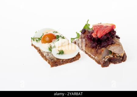 selection of open-faced Danish sandwiches (Smørrebrød) on dark rye bread. Toppings include egg, tomato, herbs, and mayo; sausage, salad, fish onions Stock Photo