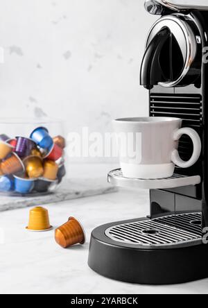 Coffee machine with espresso cup and coffee capsules pods in light kitchen background. Stock Photo