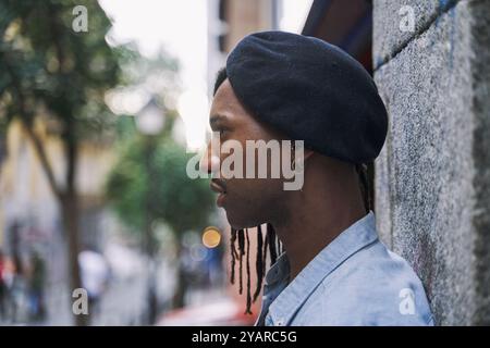 young African-American man sideways leaning against a wall wearing a sideways hat Stock Photo