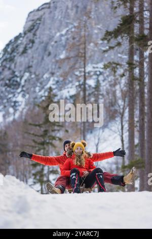 Joyful couple slides on a snow sled through a beautiful snowy forest Stock Photo
